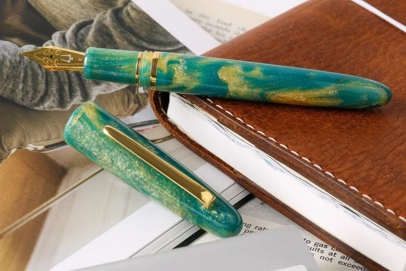 Green and gold fountain pen on a leather journal.