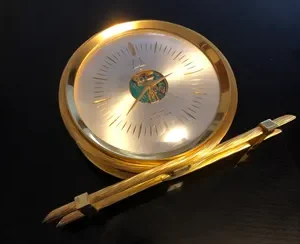 A gold clock and pencil on top of a table.