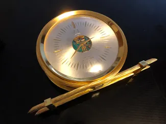 A gold clock and pencil on top of a table.