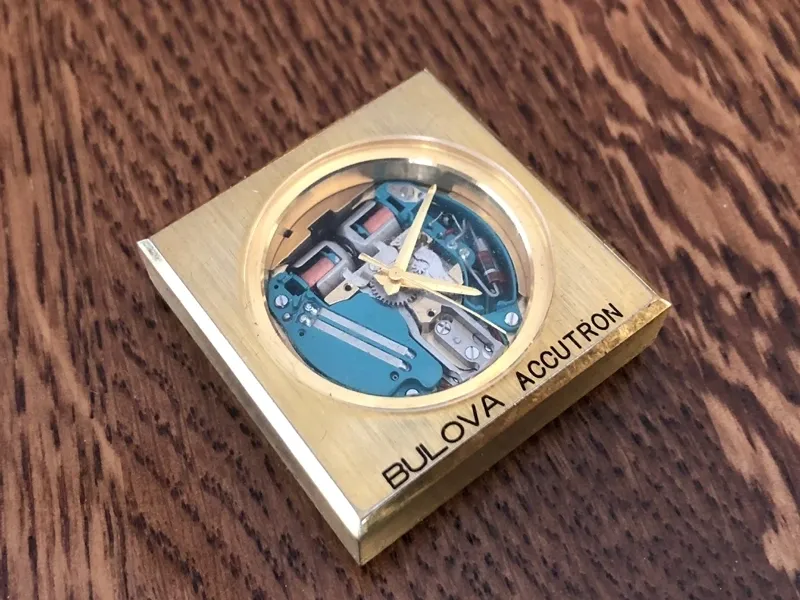 A gold square clock sitting on top of a wooden table.