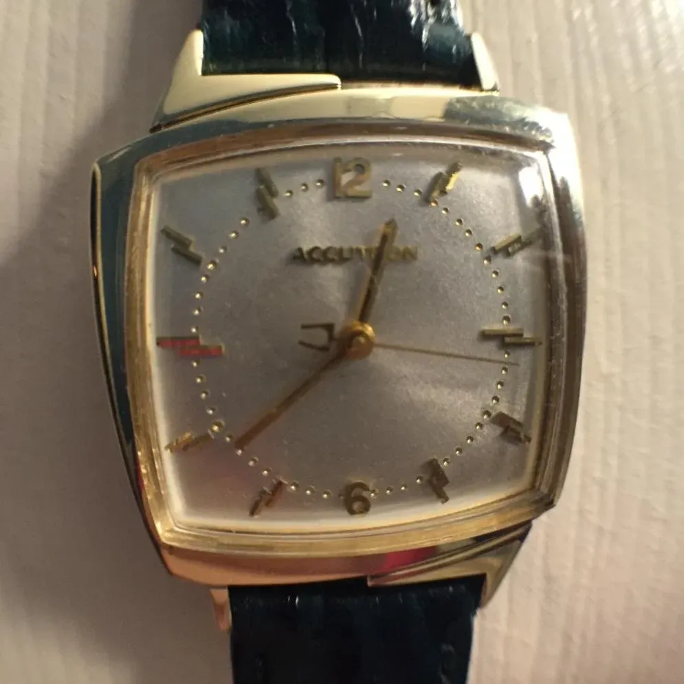 A gold watch with black leather strap on top of a table.