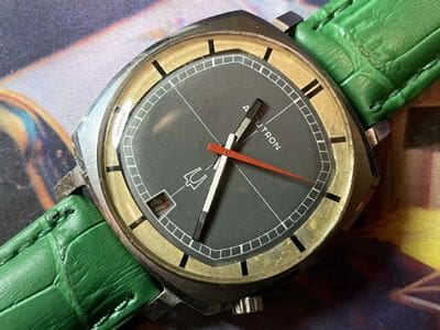 A watch with green leather strap and gold face.