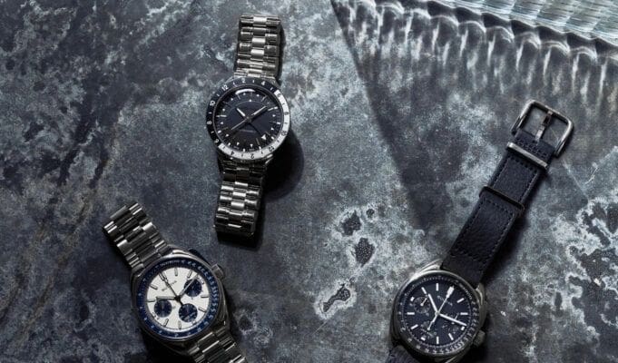 Three luxury wristwatches on a gray background.