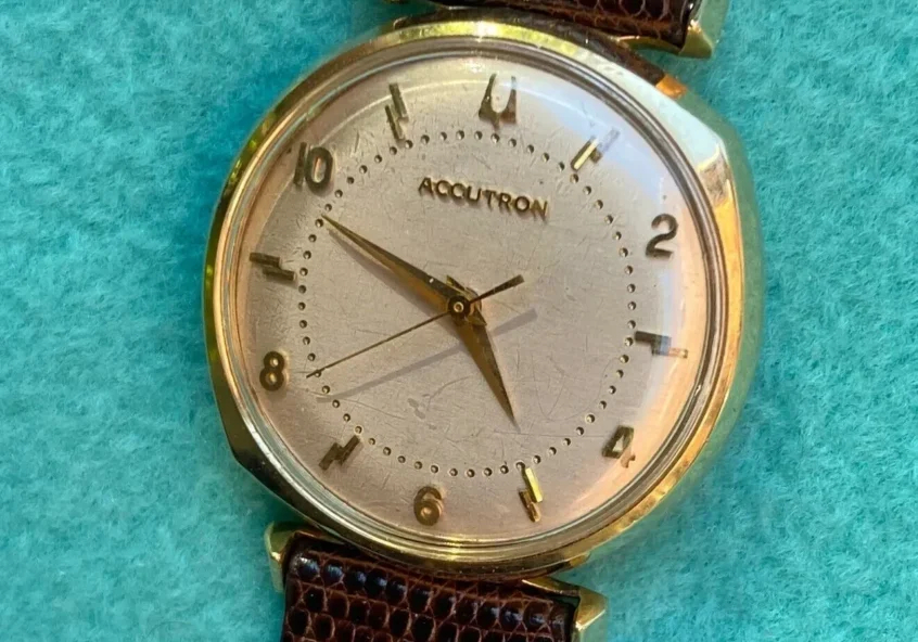 Gold Accutorn wristwatch with brown strap.