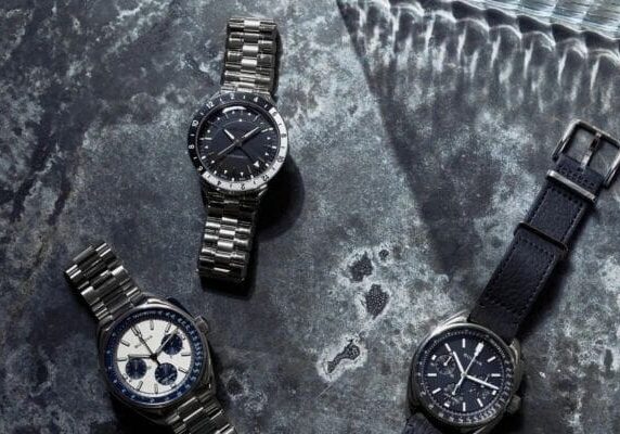 Three luxury wristwatches on a gray background.