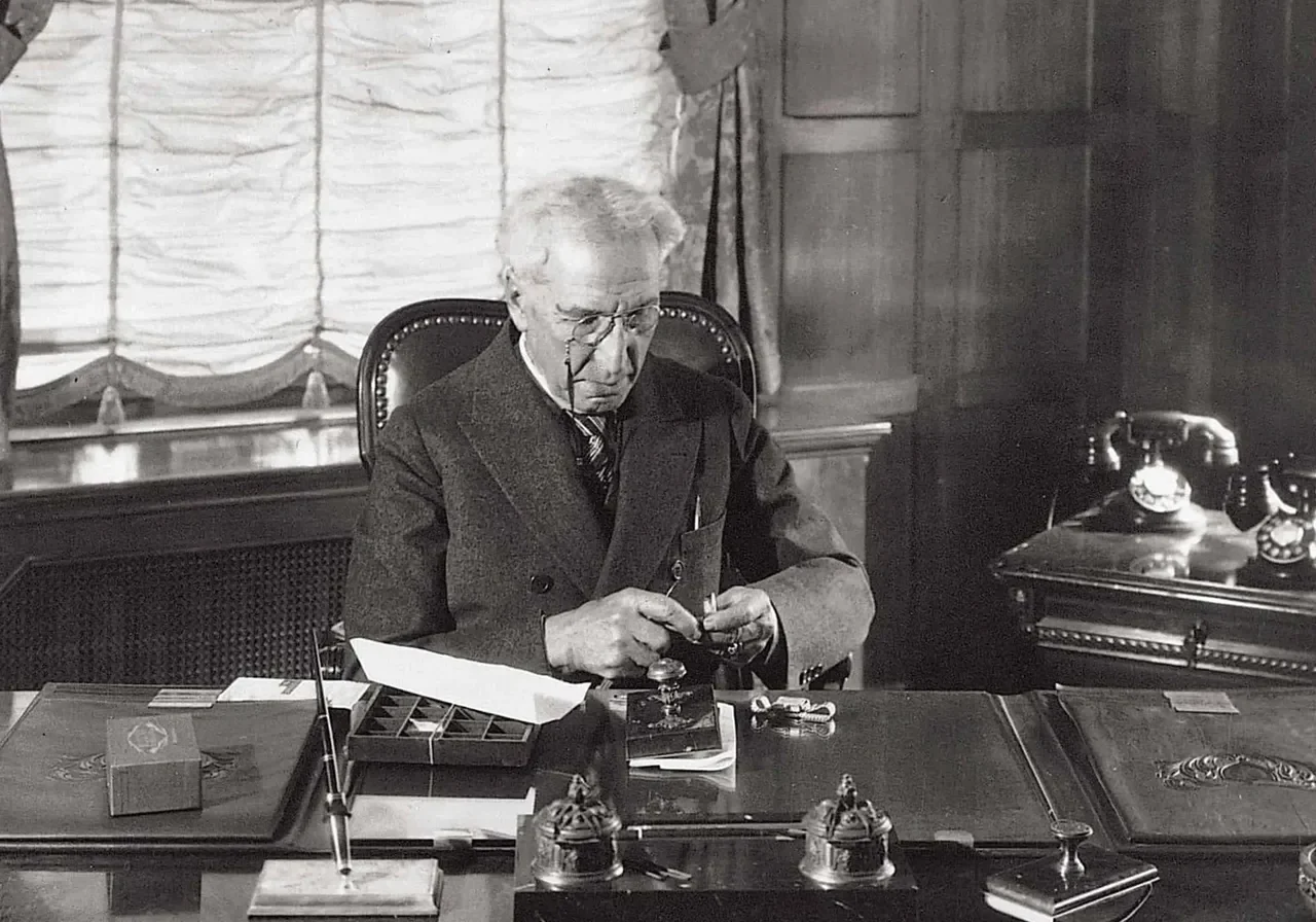 A man in a suit sits at his desk.