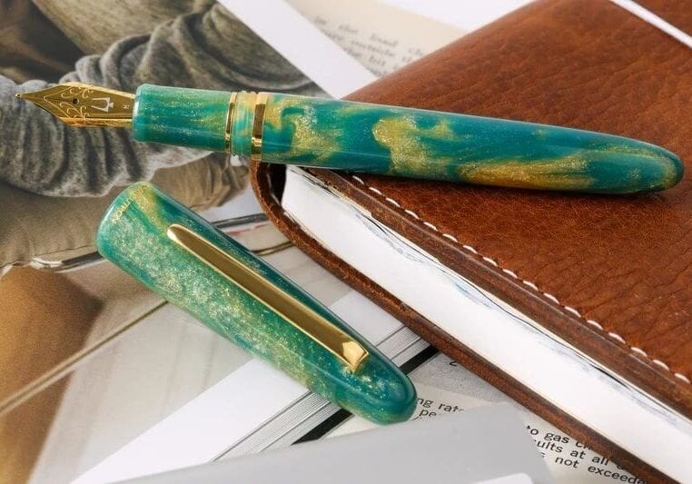 Green and gold fountain pen on a leather journal.