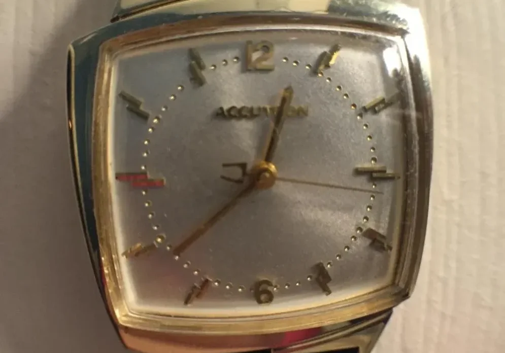 A gold watch with black leather strap on top of a table.